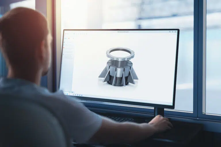 An engineer designs machine components on a computer using CAD software at a company manufacturing machines for the industry. A production hall, in the background